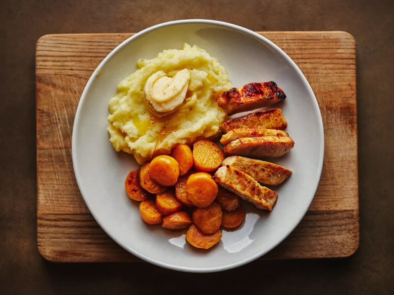 Kartoffelstock, Karottengemüse und Pouletstreifen auf einem Holzbrett